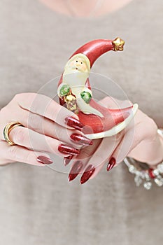 Female hands with long nails and red manicure hold a small statuette of Santa Claus