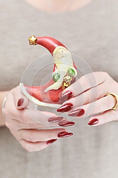 Female hands with long nails and red manicure hold a small statuette of Santa Claus
