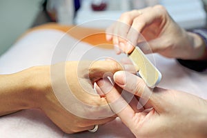 Female hands make manicure by nailfile for woman photo