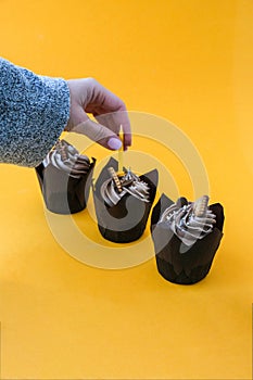 Female hands making Delicious chocolate cupcakes with cream on yellow background. Three chocolate muffin. Birthday cake