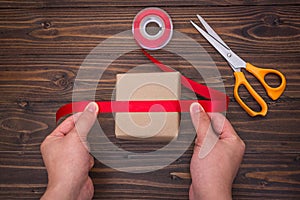 Female hands making of handmade gift box with red ribbon and sci