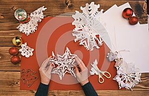Female Hands making white paper snowflakes over wooden table