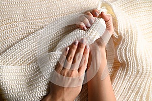 Female hands manicure close up view on white knitted sweater background. Nails care banner concept.