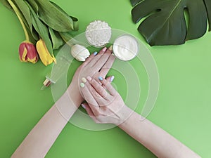 Female hands manicure beauty , spring cosmetic creative cream moisturizing , monstera tulip leaf on a background