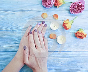 Female hands, manicure, flower rose, candle on a wooden background