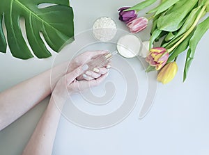 Female hands manicure, healthy cosmetic cream, spring creative tulip flower, monstera leaf on a colored background