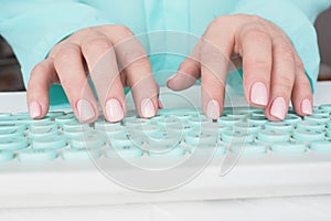 female hands with manicure and soft pink varnish on the nails are typing on the keyboard