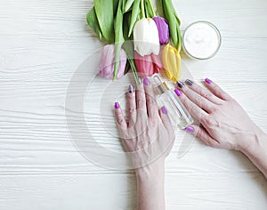 Female hands manicure treatment blossom cosmetic cream tulip flower on wooden background