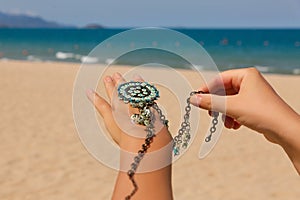 Female hands with many boho bracelets, and sand in the beach.