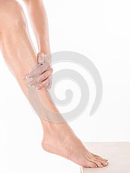 Female hands massage leg of woman with body lotion, close up