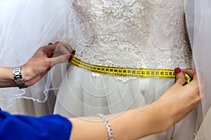 Female hands with measuring tape and wedding dress.