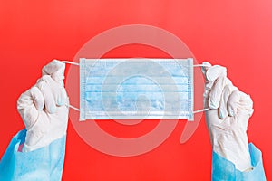 Female hands in medical gloves holding protective mask at red background. Health care concept. Coronavirus concept