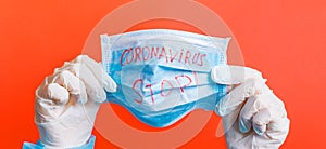 Female hands in medical gloves holding protective mask with stop coronavirus text on it at red background. Health care concept.
