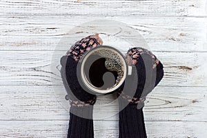 Female hands in mittens holding a cup of coffee on wooden background