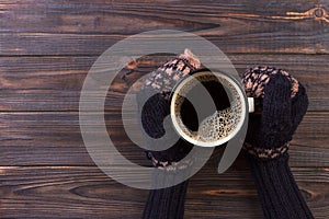 Female hands in mittens holding a cup of coffee on wooden background