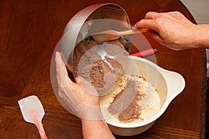 Female hands mix cocoa with dough on a wooden kitchen table. Making cake at home