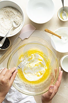 Female hands mixing eggs, sugar, oil and yogurt in glass bowl, top view. Step by step recipe of cooking a cake