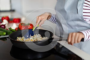 Female hands mixing rice with vegetables in frying pan