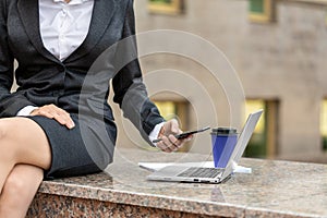 Female hands with a mobile, laptop and takeaway coffee. Faceless woman in formal wear sticks to social networks sitting