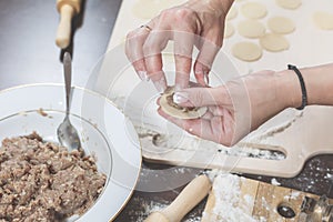 Female hands mold homemade dumplings on the background of a wooden table