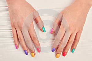 Female hands with multicolored varnish on nails.