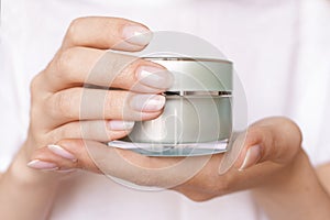 Female hands with natural manicure holding transparent cream jar. Moisturizing lotion. Skincare