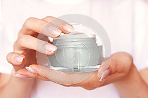 Female hands with natural manicure holding transparent cream jar. Moisturizing lotion. Skincare