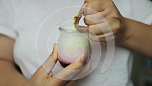 Female hands open a glass jar of fresh tasty yogurt by removing the golden foil lid in kitchen, closeup.