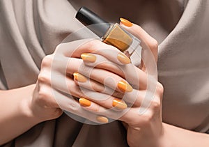 Female hands with orange nail design. Glitter orange nail polish manicure. Woman hold orange nail polish bottle