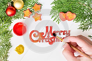 Female hands paint in red and gold dust on the inscription Merry Christmas.Christmas decoration.