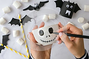 Female hands paint on white cup scary jacks face DIY for kids Halloween home activities Holiday art children craft
