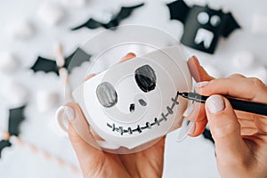 Female hands paint on white cup scary jacks face DIY for kids Halloween home activities Holiday art children craft