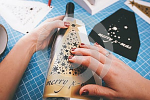 female hands with painted nails put a golden christmas ornament sticker on a wine bottle.