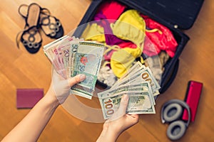 Female hands with passport Asian money and American hundred dollar bills. Suitcase with things on the floor. Choosing and exchange