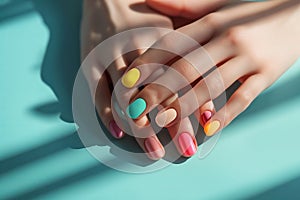 Female hands with pastel multicolored manicure elegantly crossed over a turquoise background