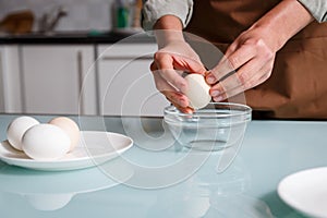 Female hands peeling off boiled egg shell on a kithcen table over glass plate