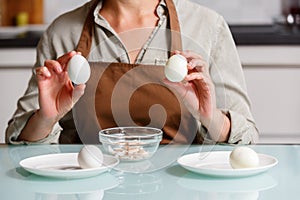 Female hands peeling off boiled egg shell on a kithcen table over glass plate