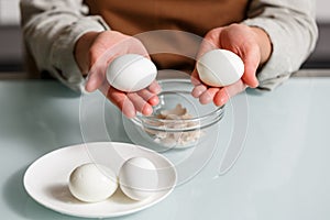 Female hands peeling off boiled egg shell on a kithcen table over glass plate