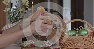 Female hands peeling off egg shell. Close-up palms of unrecognizable woman sitting at Easter table with basket and toy