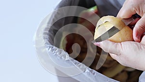 Female hands peeling potato over a trash can full of organic food waste of fruits and vegetables
