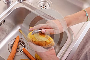Female hands peeling a potato in sink in the kitchen