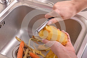 Female hands peeling a potato in sink in the kitchen