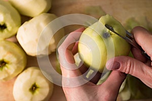 Female hands peeling skin off of green apple using a paring knife