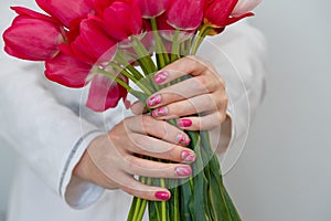 Female hands with pink spring manicure and flowers design holding tulips bouquet. Nail art, fingernails care and gel nail polish