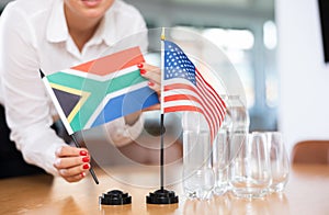 Female hands placing flags of South Africa and United States on negotiating table