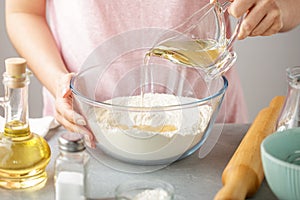 Female hands pour oil into bowl with flour, baking powder and salt.