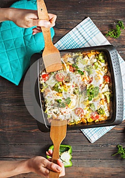 Female hands poured baked pasta with broccoli and cheesy tomato sauce on wood background