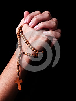 Female hands praying holding a beads rosary with a cross or Crucifix on black background