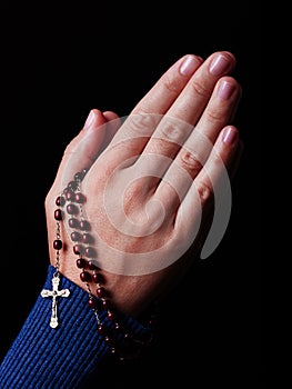 Female hands praying holding a beads rosary with Jesus Christ in the cross or Crucifix