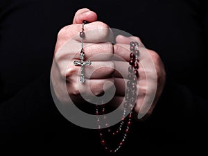 Female hands praying holding a rosary with Jesus Christ in the cross or Crucifix on black background.